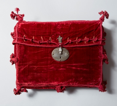 Cartera de terciopelo rojo con cordones<br/>de seda roja y borlas que penden de las<br/>esquinas, con cerradura de metal <br/>plateado, probablemente utilizada para<br/>transportar la Constitución de <br/>Cádiz de 1812 <br/>(390 x 330 x 95 mm.)
